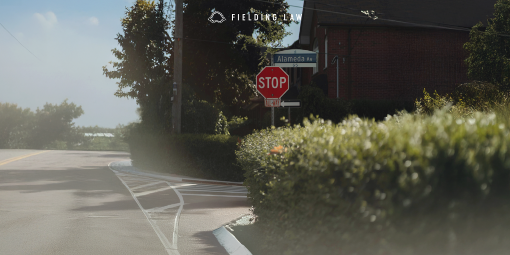 Intersection with a stop sign where a hedge is creating a blindspot for drivers and pedestrians.