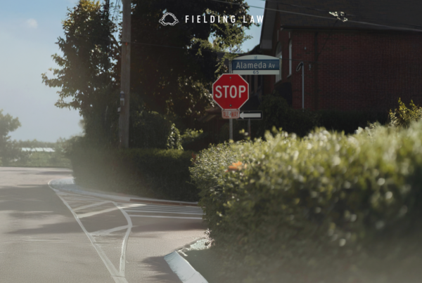 Intersection with a stop sign where a hedge is creating a blindspot for drivers and pedestrians.