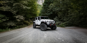 Jeep with modifications on a gravel road in the trees with a rocky mountain behind the trees