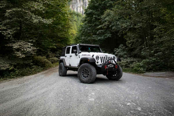 Jeep with modifications on a gravel road in the trees with a rocky mountain behind the trees