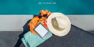 Spring break gear at the pool sitting on a chair. Including white hat, sunglasses, digital book reader, towel.