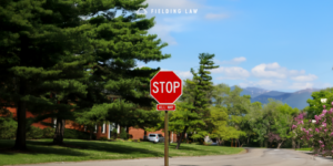 An all-way or 4-Way stop sign in a neighborhood with trees, houses, and mountains in the background