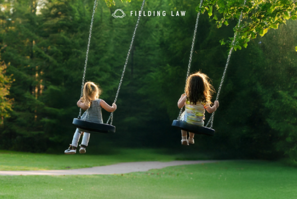 two young female friends playing in a backyard on swings with trees in the background.