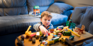 child sitting in a living room with toys all around and a sofa behind them