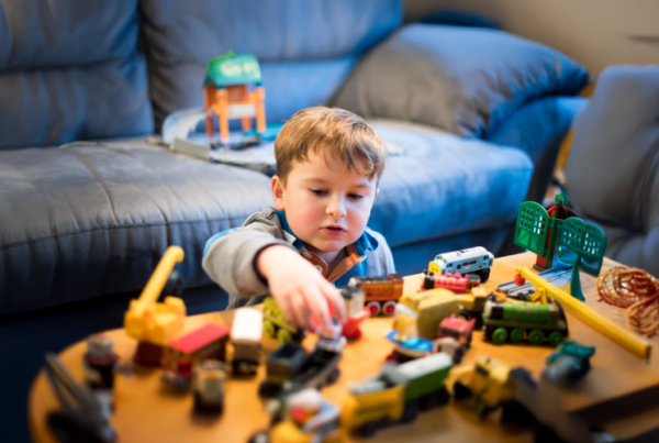 child sitting in a living room with toys all around and a sofa behind them