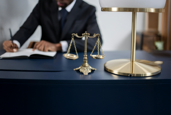 scales of justice on a navy desk with a person blurred in the background.