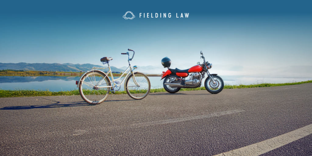 a bicycle and a motorcycle on the side of the road with a lake in the background