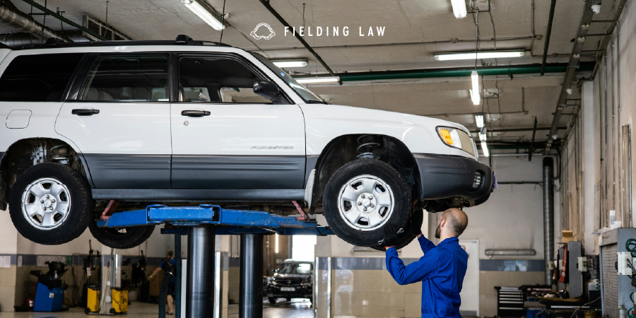 car on a lift at an auto shop with a tech looking at it after an accident claim