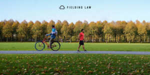 A pedestrian and a person on a bicycle passing each other on a bike path with trees in the background