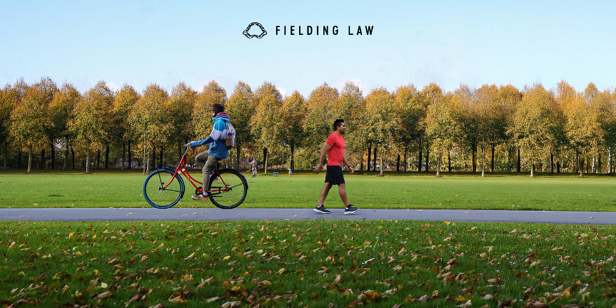 A pedestrian and a person on a bicycle passing each other on a bike path with trees in the background