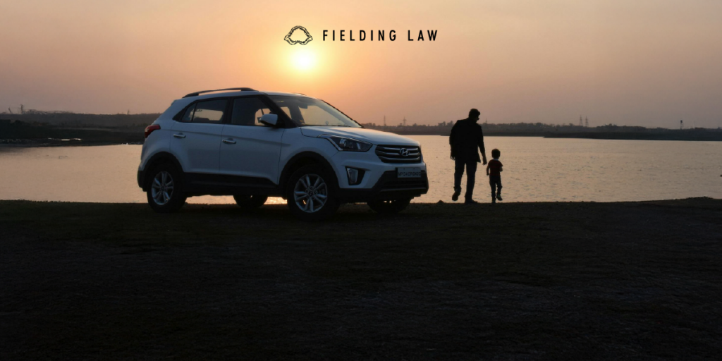 Child with an adult next to a car at sunset