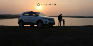 Child with an adult next to a car at sunset