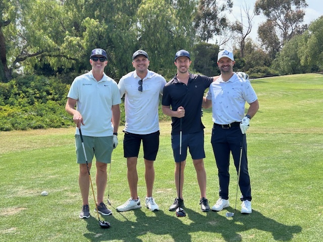 4 men standing on a golf course for a golf tournament