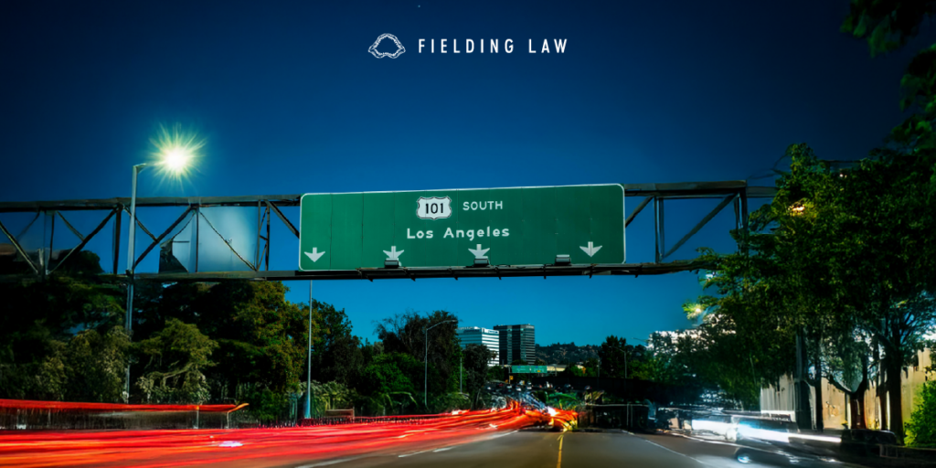 101 Freeway sign at night with cars driving under it
