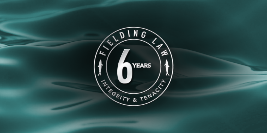 Aqua colored water background. with text that reads Fielding Law 6 Year Anniversary. Integrity & Tenacity