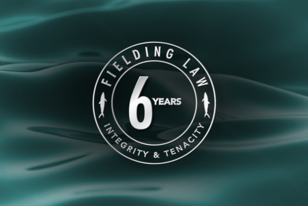 Aqua colored water background. with text that reads Fielding Law 6 Year Anniversary. Integrity & Tenacity