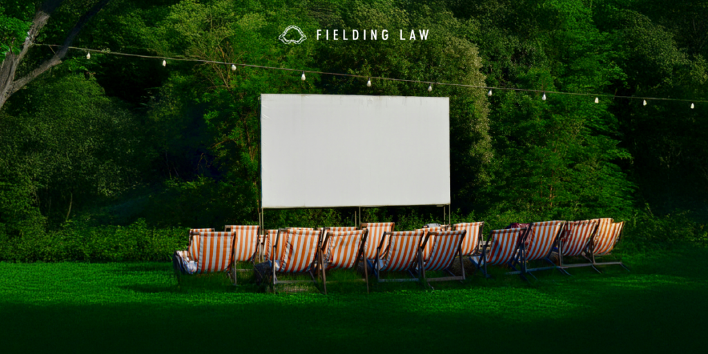 Outdoor movie screen set up with 2 rows of chairs with trees in the background