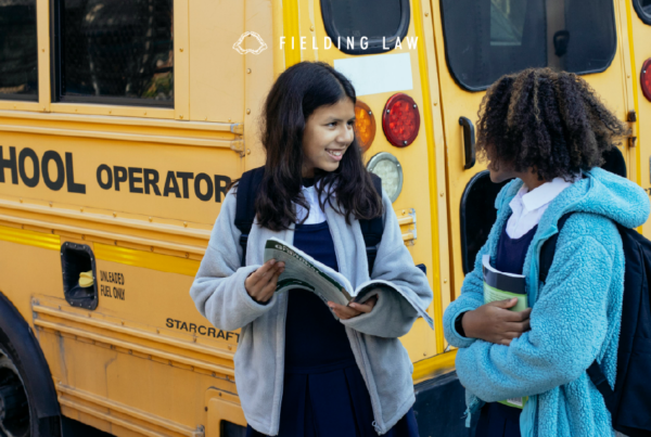 Two children standing next to a bus looking at a book