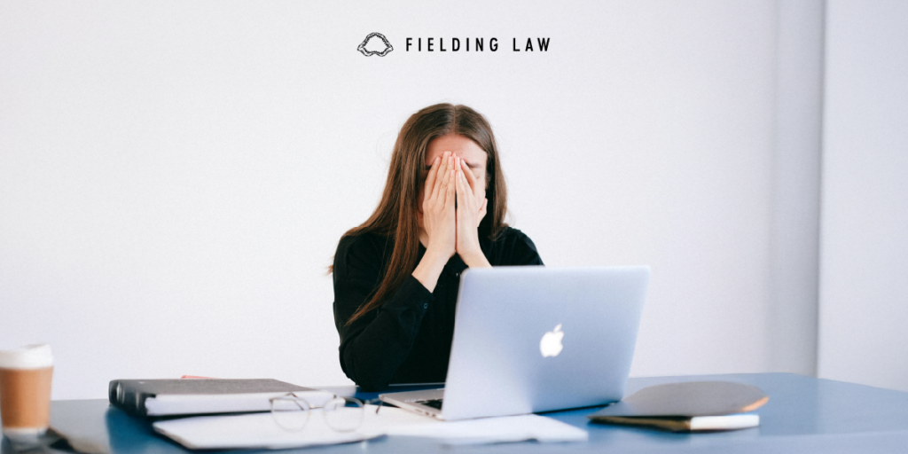 Person sitting in front of a computer screen with hands covering face in stress