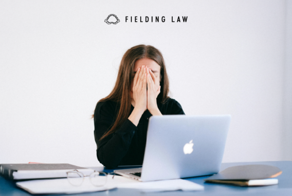 Person sitting in front of a computer screen with hands covering face in stress