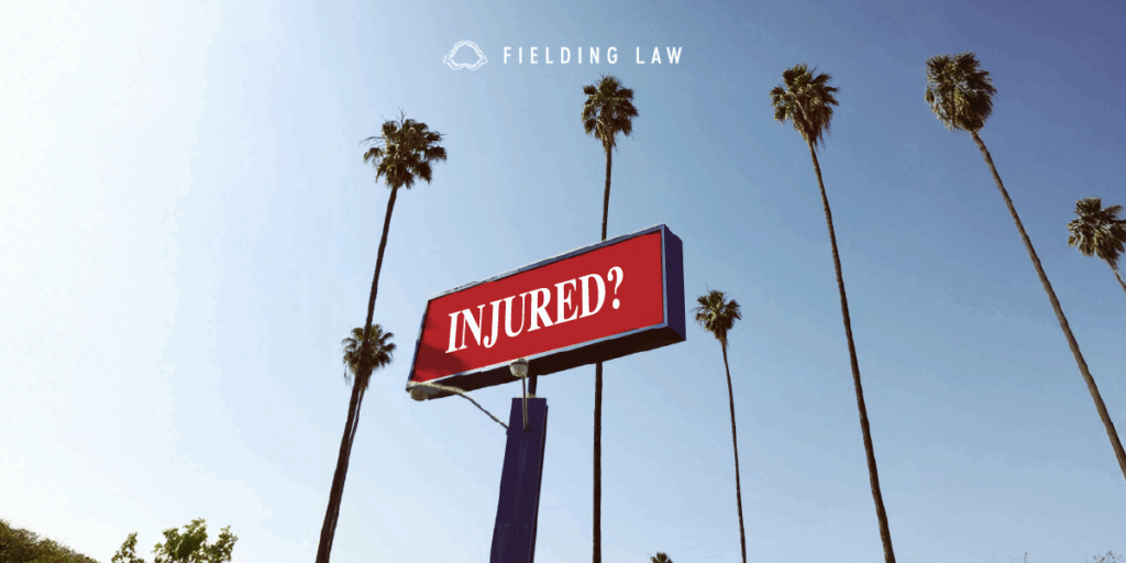 Red billboard that read Injured? with palm trees in the background