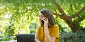 Woman on the phone talking to the insurance companies after and injury. She is sitting outside with a tree in the background