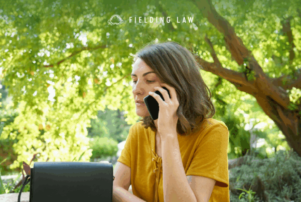 Woman on the phone talking to the insurance companies after and injury. She is sitting outside with a tree in the background