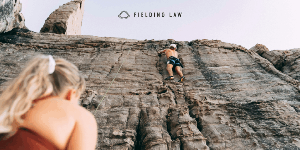 One person rock climbing another person watching from below.