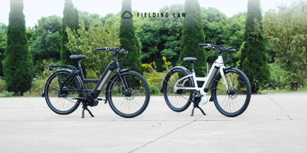 Two e-bikes standing up on a sidewalk with trees behind them