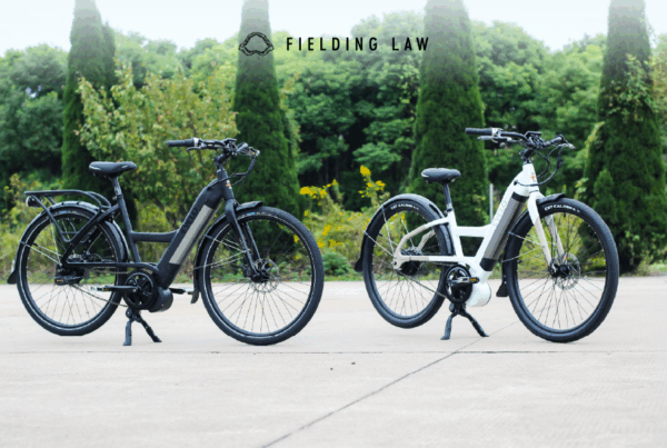 Two e-bikes standing up on a sidewalk with trees behind them