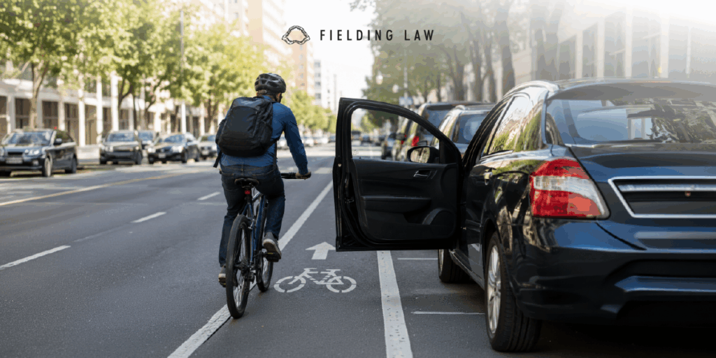 Person riding in the bike lane and a door is open on a car next to the bicycle lane